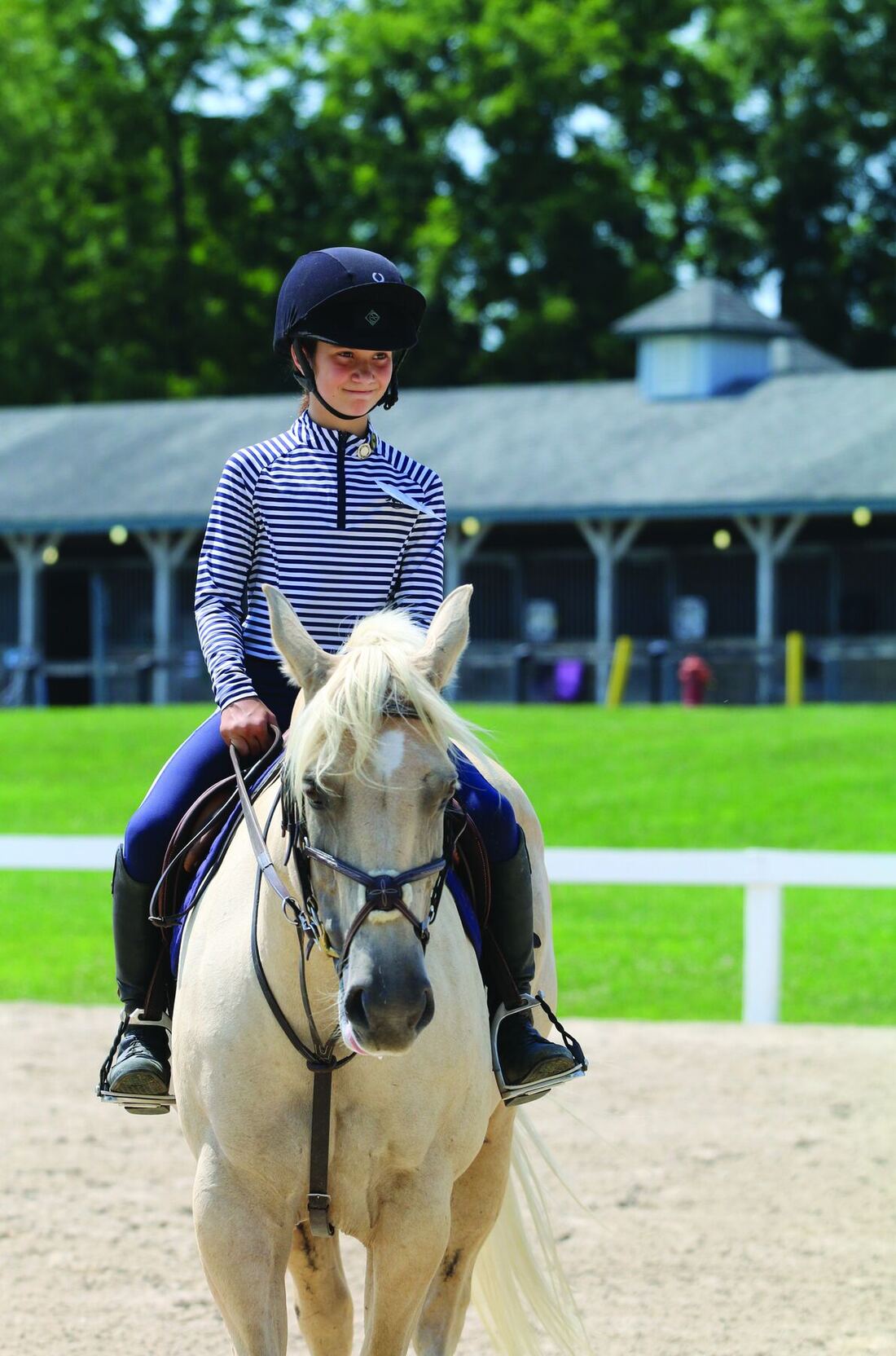 A young rider in a striped shirt on a palomino pony in an outdoor arena