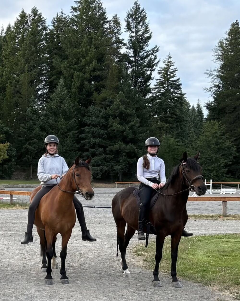 Two Baywood riders on their horses at summer camp, with tall evergreens behind them