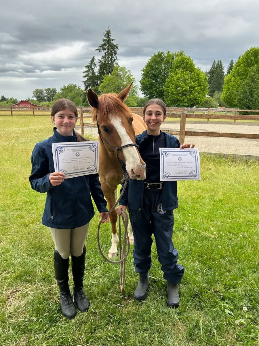 Two Baywood members holding their new certification certificates beside a chestnut horse